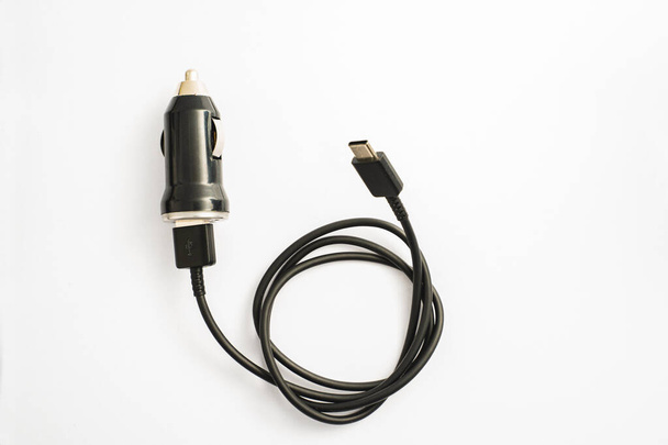schwarzes Auto-Ladegerät mit USB-Ausgang Verbindungskabel. ein Foto, aufgenommen auf einem schwarzen Autoladegerät mit USB-Anschlusskabel vor weißem Hintergrund - Foto, Bild