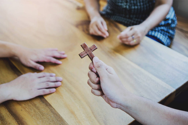 Zbliżenie Młody chrześcijanin trzyma mały drewniany krzyż w rękach, podczas gdy wyjaśnia historię Jezusa i dzielenie się Ewangelią do swoich niewierzących przyjaciół wokół drewnianego stołu wewnątrz, wielka koncepcja komisji. - Zdjęcie, obraz