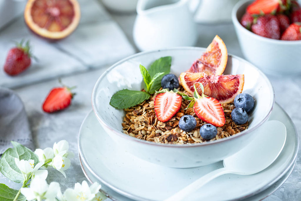 Gezond ontbijt met granola, yoghurt, fruit, bessen op een wit bord in wit bord. - Foto, afbeelding