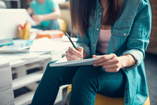 Close up of student wearing jeans holding pencil while making notes - Foto, Bild