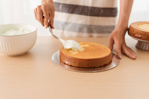 Fazendo bolo de esponja. Mão colocando cobertura em bolo recém-assado na mesa de madeira - Foto, Imagem