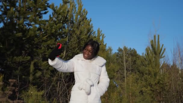 czarny kobieta robi selfie w zimie las pod jasne niebo - Materiał filmowy, wideo