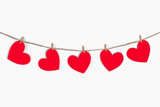 Garland of red hearts on a white isolated background. Natural rope and clothespins. The concept of recognition in love, romantic relationships, Valentines Day. Copy space - Фото, изображение