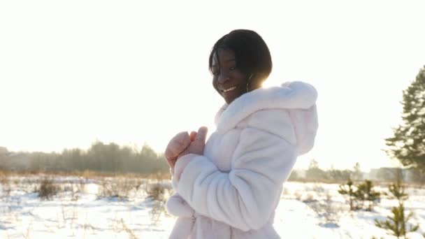 sonriente chica de piel oscura posa contra el campo cubierto de nieve vacío - Imágenes, Vídeo