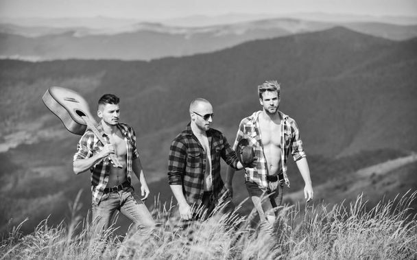 Group of young people in checkered shirts walking together on top of mountain. Men with guitar hiking on sunny day. Tourists hiking concept. Hiking with friends. Long route. Enjoying freedom together - Фото, изображение