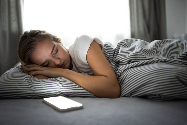 Pretty, young woman sleeping in her bed with her cell phone  - Photo, Image