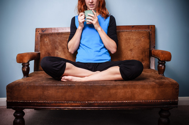 Young woman in relaxed pose is drinking tea on old sofa - Foto, afbeelding