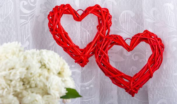 Bílé růže a dvě červená ratanová srdíčka v pozadí, zblízka. Pozadí na Valentýna, svatba, projev lásky. Mezera pro text, pohled zepředu, místo pro kopírování. - Fotografie, Obrázek