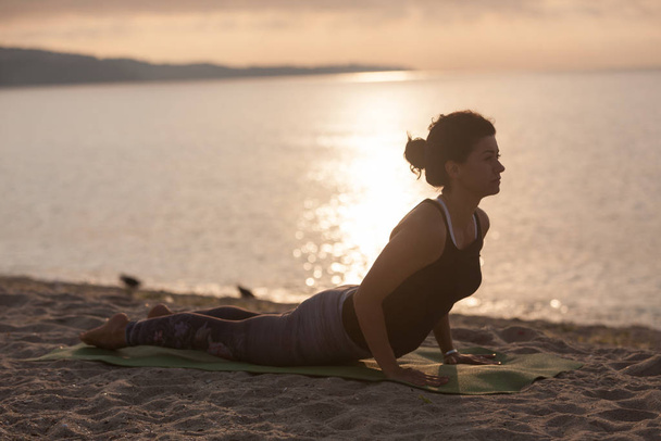 Kumsalda yoga yapan genç bir kadın. Kobra pozu, Bhujangasana. Açık hava sporları. Sağlıklı yaşam. - Fotoğraf, Görsel