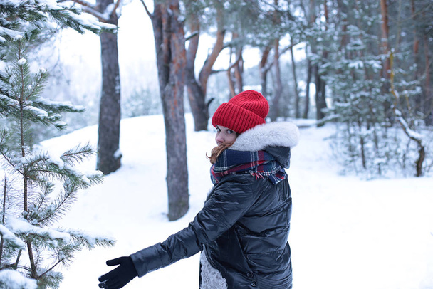 Piękna dziewczyna z zielonymi oczami i rudymi włosami w czerwonym kapeluszu na spacerze w zimowym śnieżnym lesie - Zdjęcie, obraz