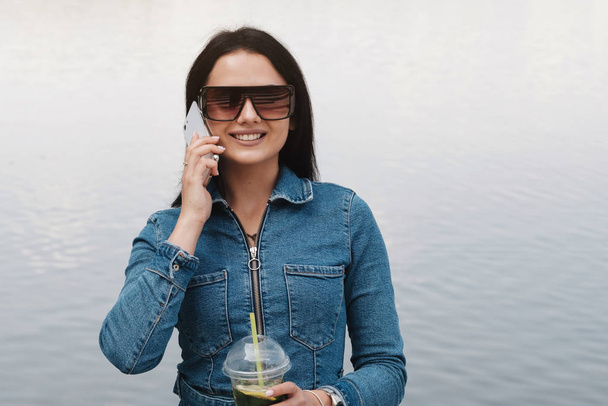 Une belle fille brune habillée en salopette de jeans utilise un smartphone, concept de communication
 - Photo, image