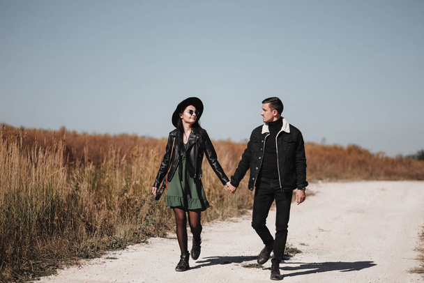 Retrato de pareja feliz vestida con ropa negra elegante disfrutando de un buen rato caminando en el campo
 - Foto, Imagen