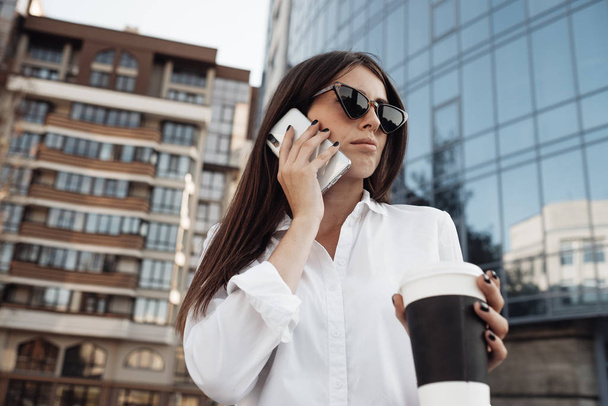 Portrait of One Fashionable Girl Dressed in Jeans and White Shirt Drinking Coffee and Using Her Smartphone, Business Lady, Woman Power Concept - Foto, Imagem