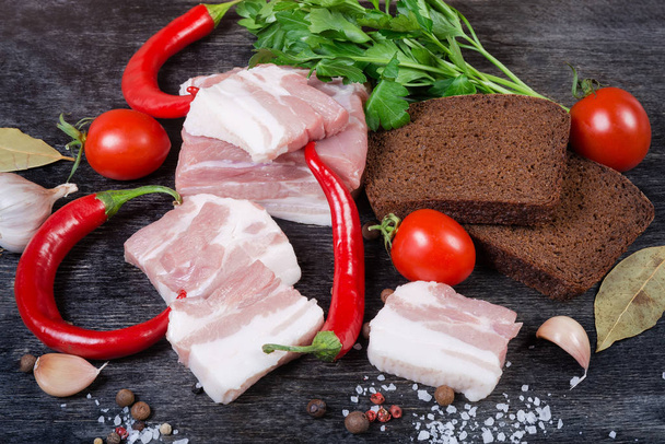 Pork belly slices among chili, cherry tomatoes, spices, brown bread - Фото, изображение