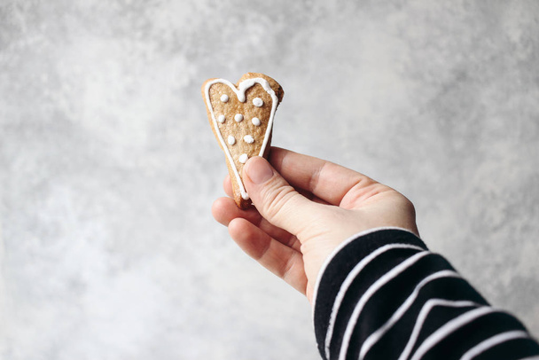 Female hand holding ginger bread heart cookie with white icing. Valentine or Mothers day holiday day composition. Love concept. Grunge blurred background with negative space. - Photo, Image