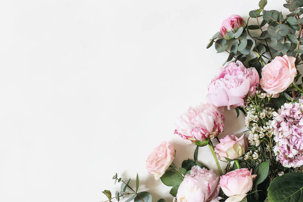 Beyaz arka planda pembe güller, ortanca, şakayık, çiçek ve okaliptüs yaprakları ve dallarıyla kadınsı bir foto. Düz yerde, üst tarafta. Çiçek çerçevesi, botanik dekoratif köşesi.. - Fotoğraf, Görsel
