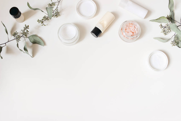 Styled beauty frame, web banner. Skin cream, shampoo bottle, dry eucalyptus leaves and pink Himalayan salt. White table background. Organic cosmetics, spa concept. Empty space, flat lay, top view. - Foto, Bild