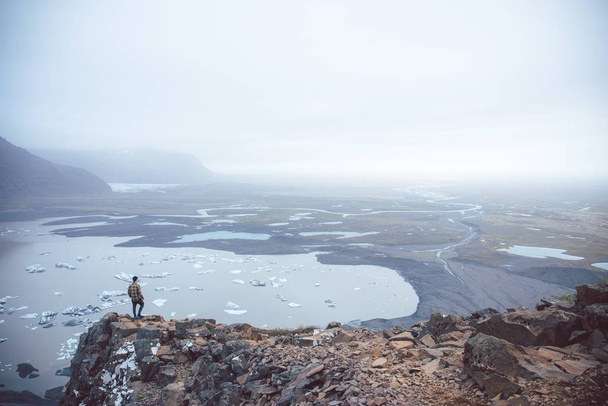 An aerial shot of a person standing on a cliff overlooking the lakes in the fog captured in Iceland - Foto, imagen