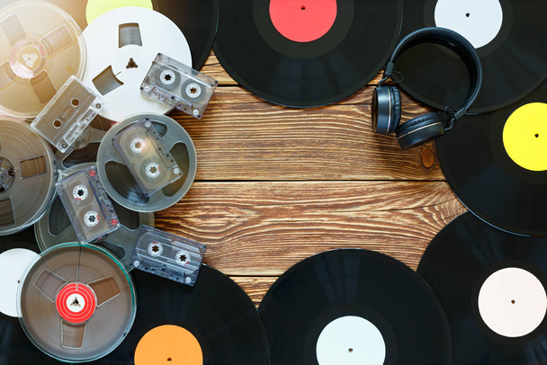 Old vintage bobbins, vinyl records, cassette tapes and headphones on a wood table background. Multicolored labels. Top view. Place to copy space. Sun glare. - Photo, Image