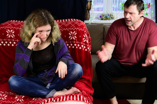 Η έννοια των οικογενειακών προβλημάτων του πατέρα και της ενήλικης κόρης σε ένα σακάκι και τζιν κάθονται σε έναν καναπέ μπροστά από την κάμερα στο εσωτερικό του σπιτιού. Φωτογραφία ενός δυσαρεστημένου άνδρα και μιας νεαρής γυναίκας. - Φωτογραφία, εικόνα
