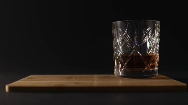 Glass of whiskey on a cutting board against a black blurry background - Фото, изображение