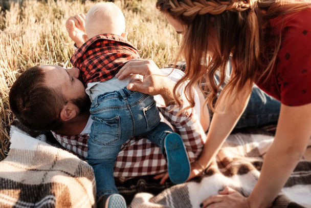 Happy Young Family Mom and Dad with Their Little Son Enjoying Summer Weekend Picnic Outside the City in the Field at Sunny Day Sunset, Vacation Time Concept - 写真・画像