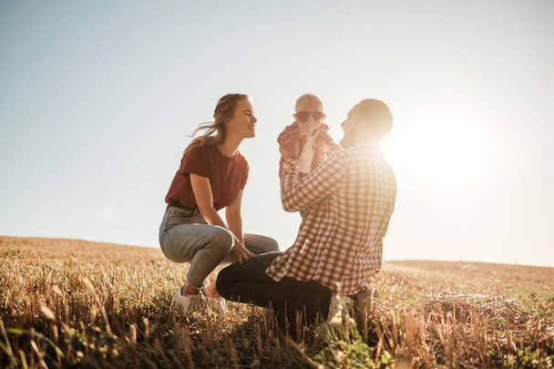 Szczęśliwa młoda rodzina mama i tata z ich małym synem korzystających letni weekend piknik poza miastem na polu w słoneczny dzień zachód słońca, wakacyjny czas Concept - Zdjęcie, obraz