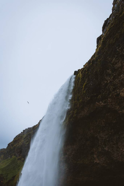A vertical low angle shot of a beautiful waterfall on the rocky cliffs captured in Iceland - Photo, image