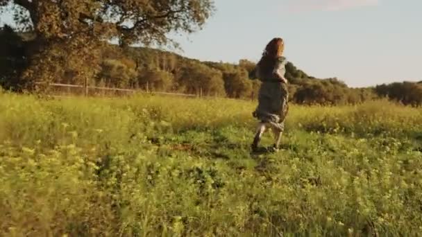 Girl in green dress walks running through the fields fool of blooming yellow flowers. Long hair woman running around the beautiful countryside. Golden light in idyllic landscape. Peace and tranquility - Materiaali, video
