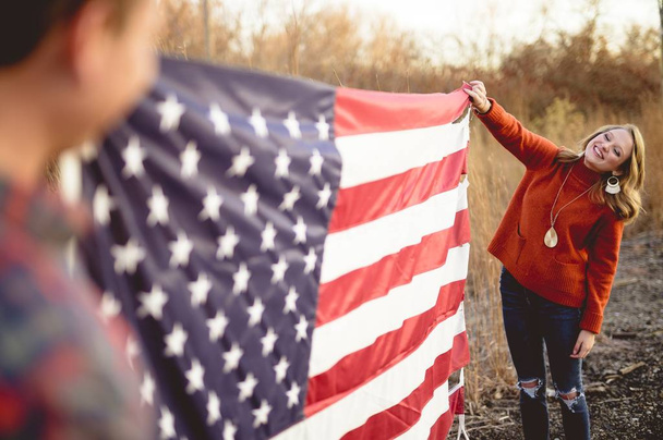Couple holding the American flag white standing near the railway - Zdjęcie, obraz