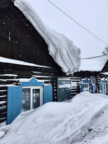 Veel sneeuw op het dak van het huis en de gebouwen. Winter op het platteland en in de stad. - Foto, afbeelding