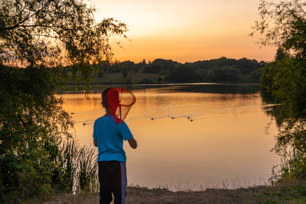 Маленький мальчик с сетью в руках стоит у озера любуется
 - Фото, изображение
