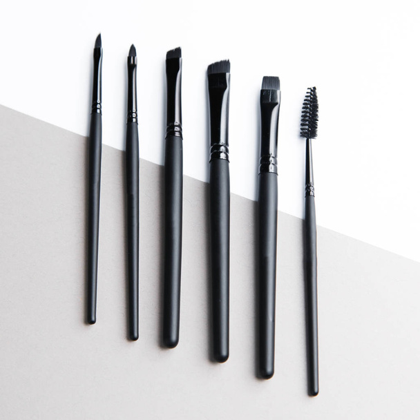  Light double background for the site. Tools for makeup artist. A set of makeup brushes. Black plastic eyebrow brush. - Foto, imagen