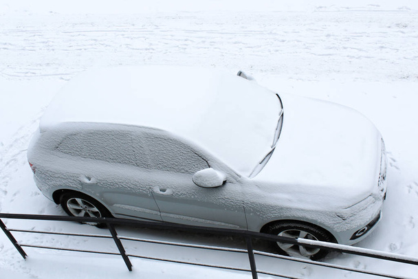 駐車場の冬の吹雪の中で雪で覆われた車 - 写真・画像