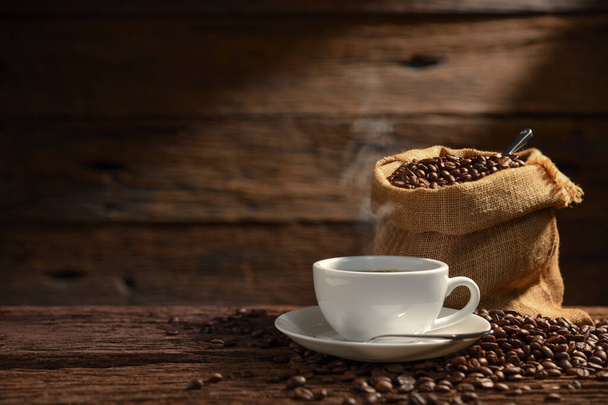 Cup of coffee with smoke and coffee beans on old wooden background - Фото, изображение
