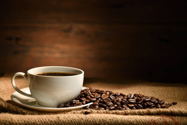 Kopje koffie en koffiebonen op jute zak op oude houten achtergrond - Foto, afbeelding
