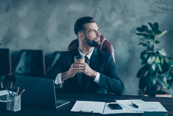 Photo of successful business guy hold takeout coffee beverage mug thoughtfully look window enjoy pleasant drink wear black blazer shirt tie suit costume sit chair office indoors - Foto, afbeelding