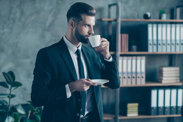 Profile photo of successful business guy self-confident person hold coffee beverage mug plate look window thoughtful wear black blazer shirt tie suit costume standing office indoors - 写真・画像
