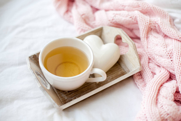 Beautiful white cup with tea on the bed, pink knitted plaid, decor Valentine's Day. Breakfast in bed. Morning. Spring. Cozy. - Photo, Image