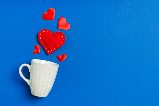 Feiertagskomposition aus roten Herzen, die aus einer Tasse auf buntem Hintergrund herausfallen. Draufsicht auf das Valentinstag-Konzept mit Kopierraum - Foto, Bild