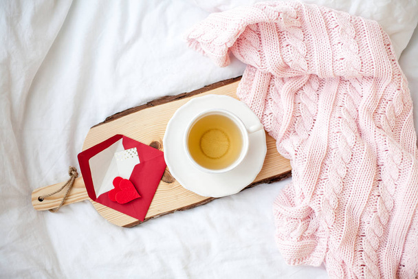 Piękny biały kubek z herbatą na łóżku, różowa dzianina w kratę, pocztówka Happy Valentine 's Day. Śniadanie do łóżka. Dzień dobry. Wiosną. Przytulne. - Zdjęcie, obraz