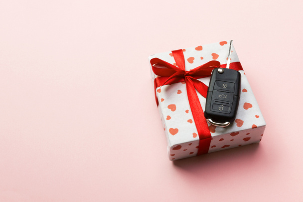Dare regalo auto chiave concetto vista dall'alto. Scatola regalo con fiocco nastro rosso, cuore e chiave auto su sfondo color corallo
 - Foto, immagini