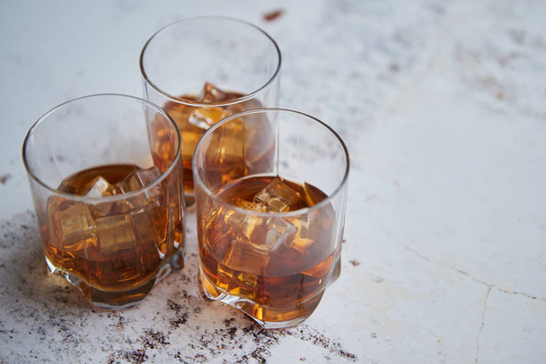 Three glasses filled with ice cubes and old aromatic whiskey - Фото, изображение