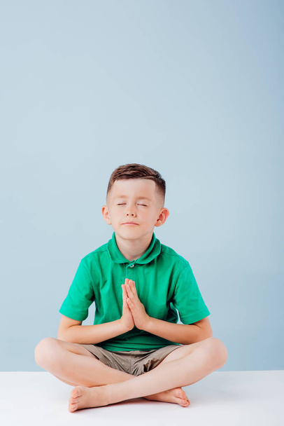 little boy practicing yoga, isolated on blue background, copy space, in studio - Valokuva, kuva
