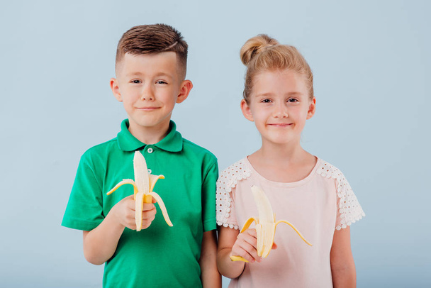 two children with bananas in hand. girl and boy. isolated on blue background, copy space, in studio, positive facial emotions - Foto, Bild