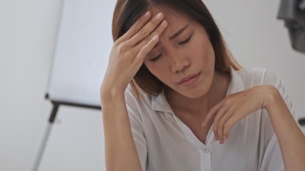 Disappointed sad asian business woman touching her head while sitting by the table in the office - Video