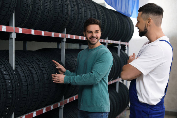 Mechanic helping client to choose car tire in auto store - Фото, зображення