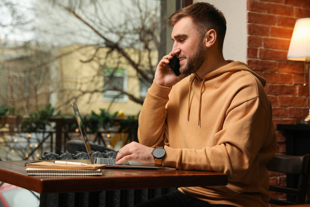 Male blogger talking on phone in cafe - Фото, изображение
