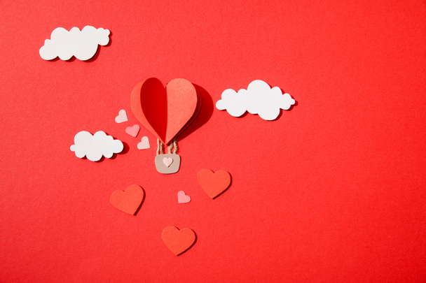 top view of paper heart shaped air balloon in clouds on red background - Фото, изображение