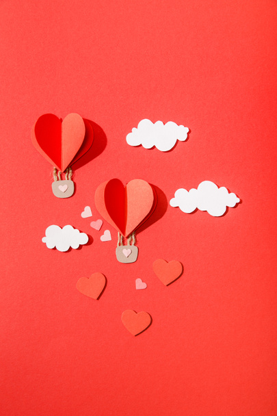 κορυφαία άποψη του χαρτιού μπαλόνια αέρα σχήμα καρδιάς στα σύννεφα σε κόκκινο φόντο - Φωτογραφία, εικόνα